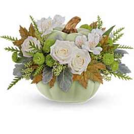 White roses in a pale green pumpkin-shaped container with autumn leaves