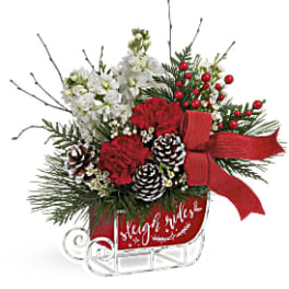 Christmas arrangement with red flowers, white blooms, pinecones, and a red bow in a sleigh
