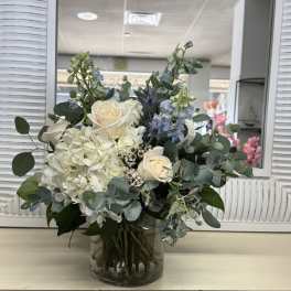White roses and hydrangea in a glass vase with blue flowers and eucalyptus