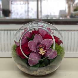 Pink orchids and red roses in a clear round glass vase