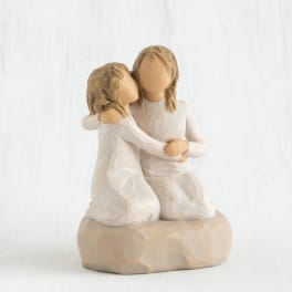 Two faceless figurines in white dresses embracing on a beige base
