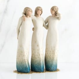 Three faceless figurines in long cream dresses with blue-speckled hems