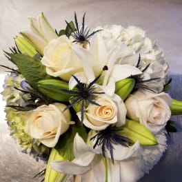 White roses and lilies arranged with pale hydrangea and dark blue thistle
