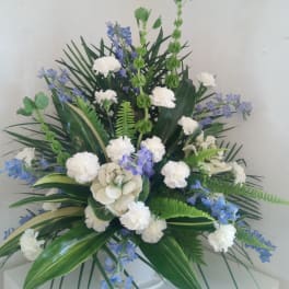 White carnations and blue flowers in a white vase with tropical foliage