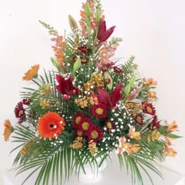 Tall mixed floral arrangement in a white vase with orange and burgundy blooms