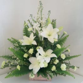White lilies and small white flowers arranged in a wooden box with fern foliage