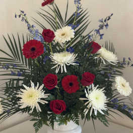 Red roses and white daisies in a white vase with blue accents