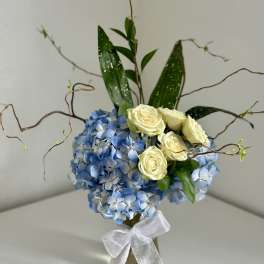 Blue hydrangea arrangement with cream roses in a glass vase