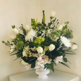 White floral arrangement in a white vase with roses and orchids