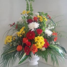 Mixed bouquet in a white pedestal vase with red, yellow, orange, and white flowers