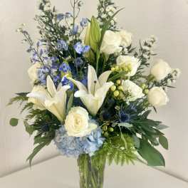 White lilies, roses, and blue flowers in a clear glass vase