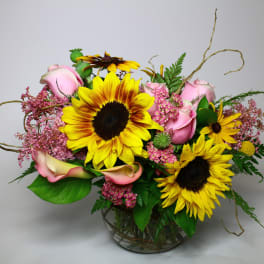 Bouquet of sunflowers, pink roses, and calla lilies in a glass vase