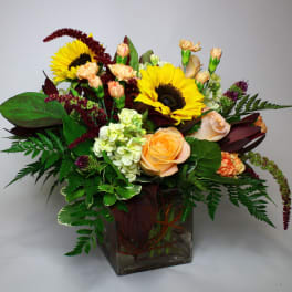 Bouquet of sunflowers, roses, and carnations in a square glass vase