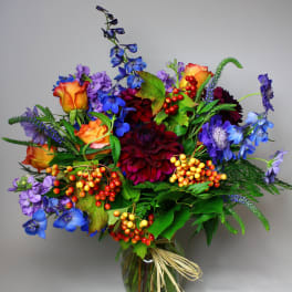 Colorful mixed bouquet in a glass vase with orange roses and blue flowers