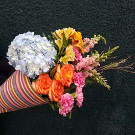 Mixed bouquet with blue hydrangea, orange roses, and pink flowers in striped wrap