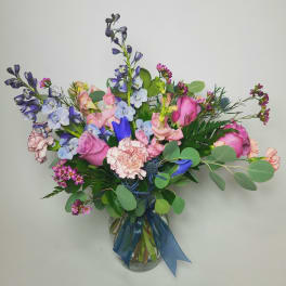 Mixed bouquet of pink and blue flowers in a glass vase with a blue ribbon
