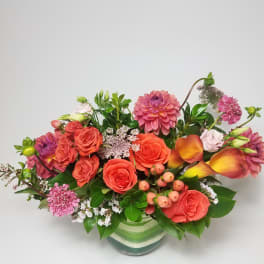Mixed bouquet of orange and pink flowers in a striped glass vase