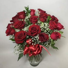 Bouquet of red roses with baby's breath in a clear glass vase and red ribbon