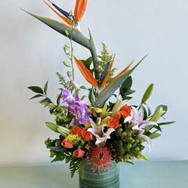 Tropical bouquet with orange bird of paradise and lilies in a glass vase