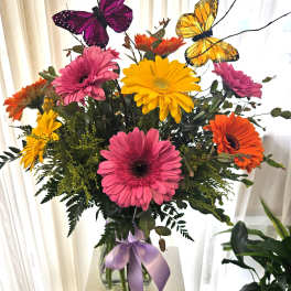Bouquet of colorful gerbera daisies in a glass vase with butterfly picks