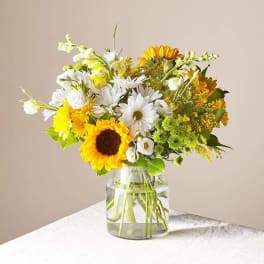 Bouquet of sunflowers, white daisies, and yellow flowers in a glass vase