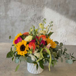 Mixed bouquet in a white textured vase with sunflowers and bright pink blooms
