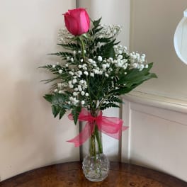 Single pink rose with baby's breath in a clear glass vase tied with a pink ribbon.