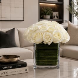 White rose arrangement in a clear square vase on a table
