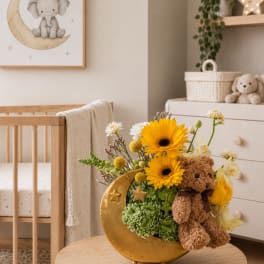 Yellow gerbera bouquet in a gold crescent vase with a teddy bear