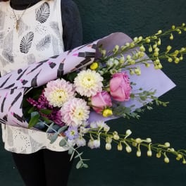Handheld bouquet of pink and white flowers wrapped in lavender paper