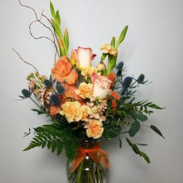 Orange and cream floral arrangement in a glass vase with a ribbon