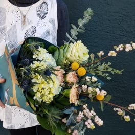 Handheld bouquet with pale flowers and white berries in teal wrapping