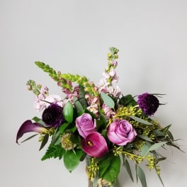 Pink roses and calla lilies in a glass vase with purple blooms