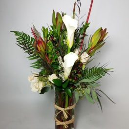 Tall arrangement of white calla lilies and red tropical blooms in a glass vase