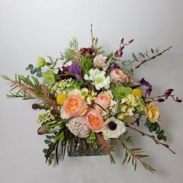 Mixed bouquet with peach, white, purple, and yellow flowers in a glass vase