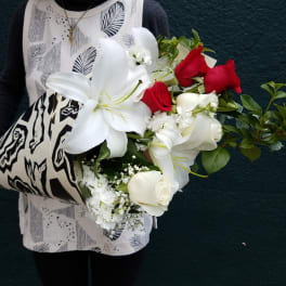 Bouquet of white lilies, red roses, and white calla lilies wrapped in patterned paper