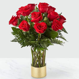 Red roses arranged in a clear glass vase with a gold base
