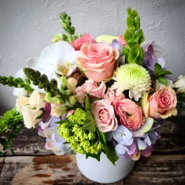 Bouquet of pink roses, white orchids, and green blooms in a white vase