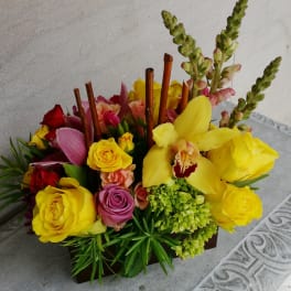 Bright mixed bouquet with yellow roses and orchids in a low wooden container