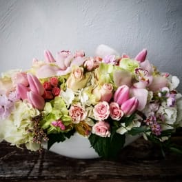 Low floral arrangement of pink roses, tulips, and pale hydrangeas in a white bowl