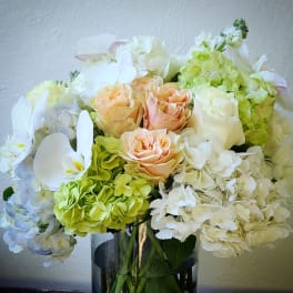 Bouquet of peach roses, white orchids, and pale hydrangeas in a glass vase