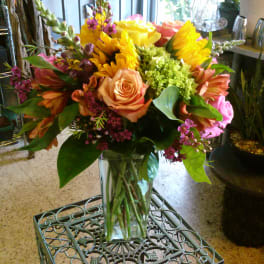 Mixed bouquet of roses, sunflowers, and pink blooms in a glass vase