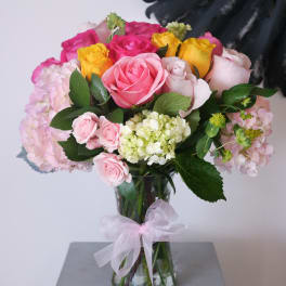 Bouquet of pink, yellow, and white roses in a glass vase with a ribbon