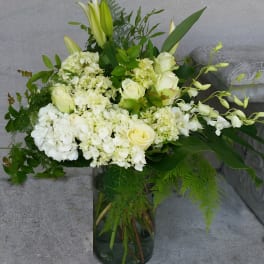 White floral arrangement in a glass vase with lilies, roses, and orchids
