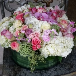 Round arrangement of pink and white roses, hydrangeas, and orchids in a green container