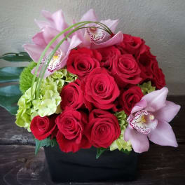 Red roses and pale pink orchids in a black container