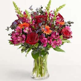 Bouquet of red roses, pink alstroemeria, and orange daisies in a clear glass vase