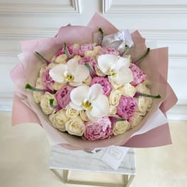 Bouquet of pink and cream flowers with white orchids wrapped in blush paper