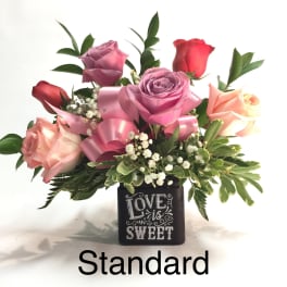 Pink and red roses in a black vase with a "Love is Sweet" design