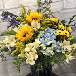 Mixed bouquet with sunflowers, blue hydrangeas, and white alstroemeria in a dark vase